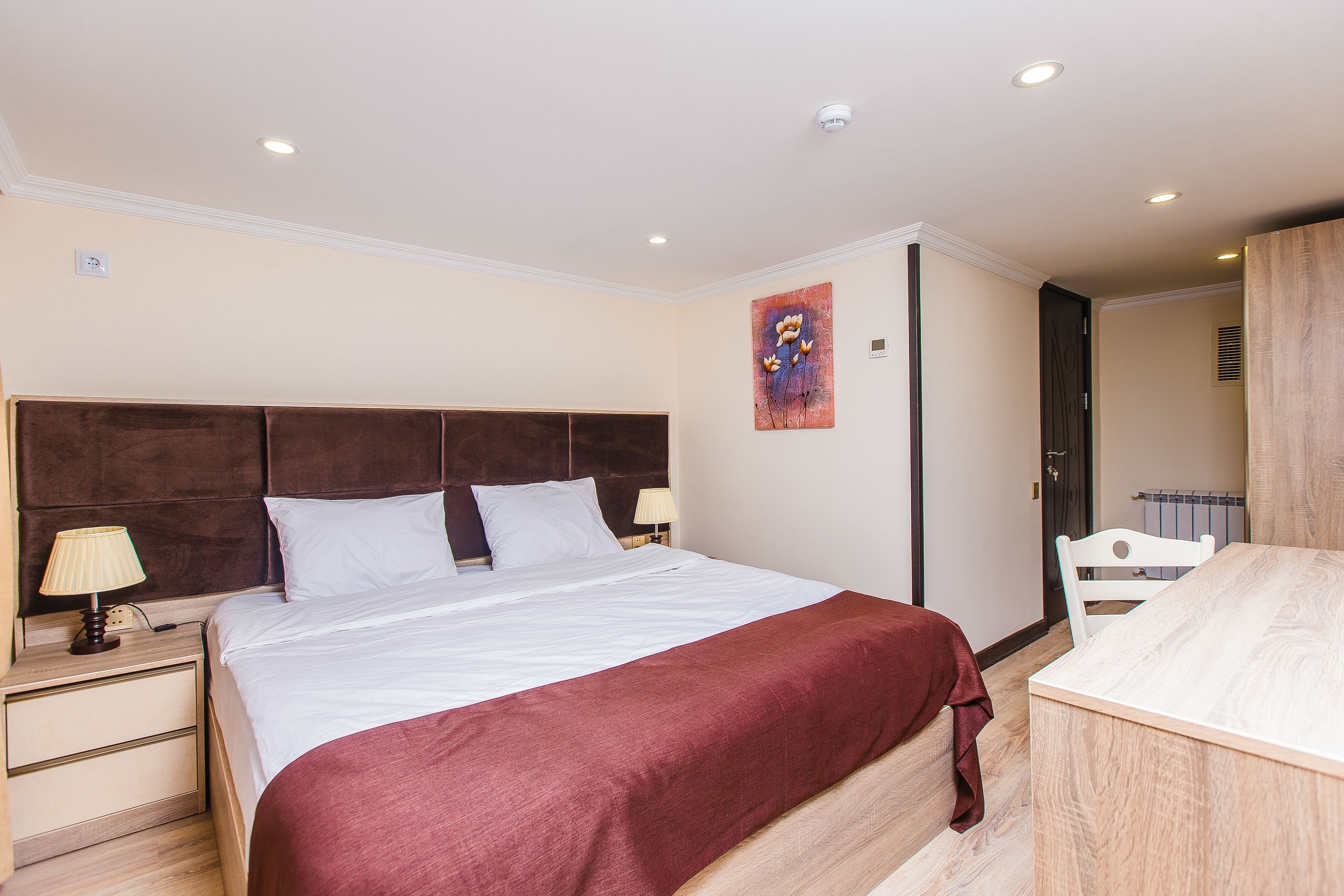 A bedroom with a bed, bedside tables, a lamp, a painting, and a wooden desk.