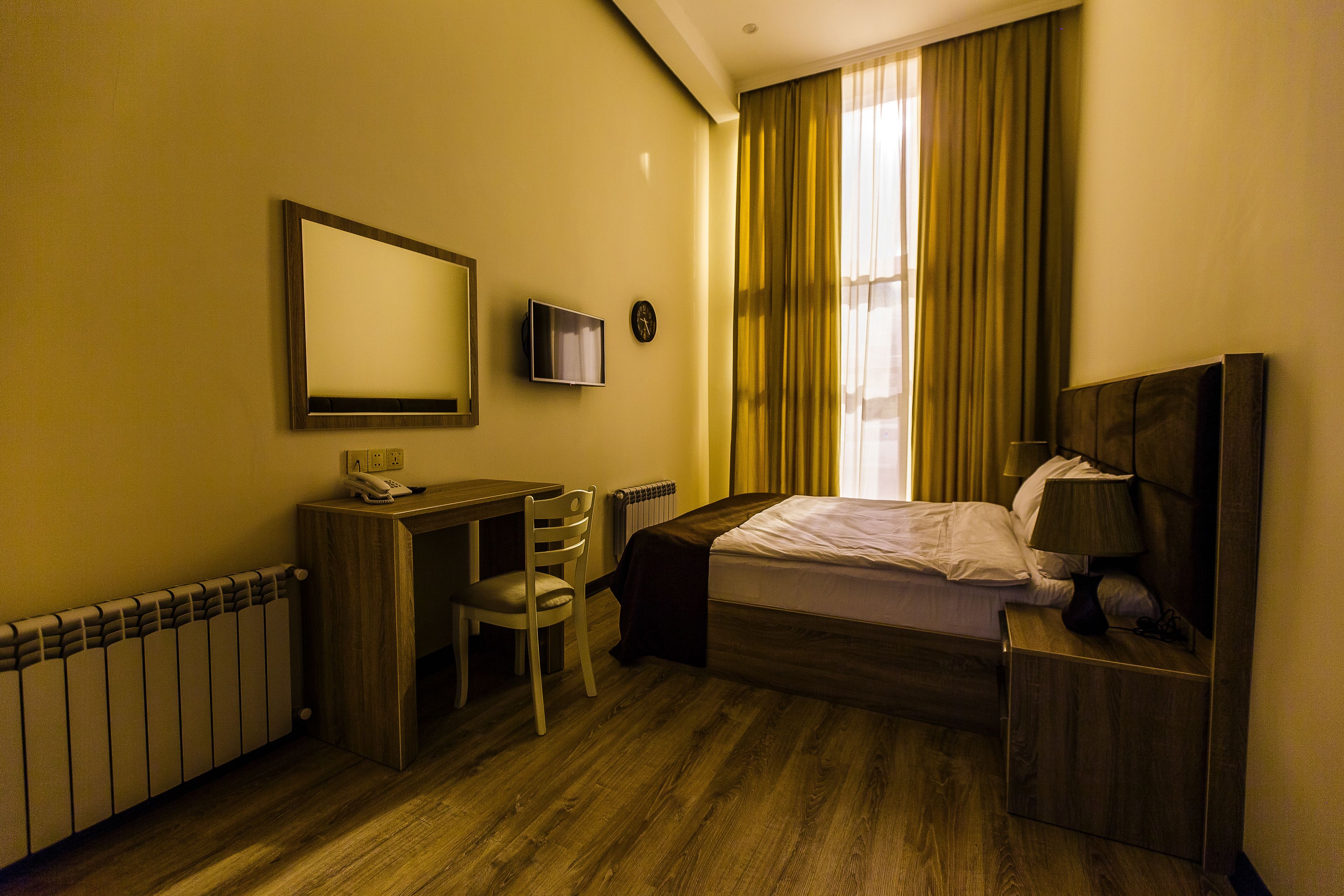 Habitación de hotel con cama, escritorio, silla, televisión y ventana con cortinas.