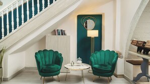 A staircase with white balusters, a teal accent wall, a round table with a white marble top, and two green armchairs. - Elia Palazzo Hotel (Chania)