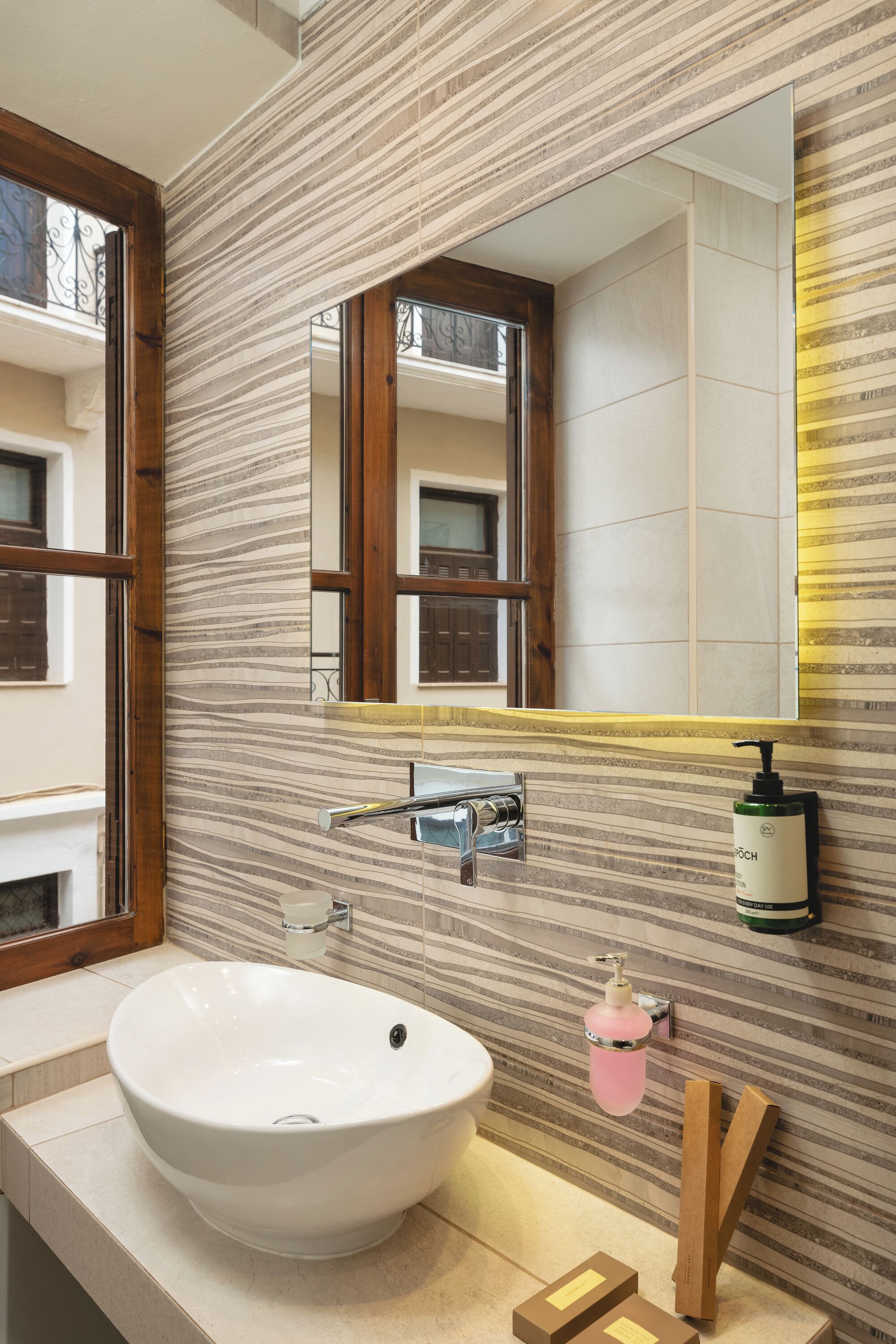 Une salle de bain avec un grand lavabo blanc, un miroir avec un cadre en bois et un pare-chocs mural à rayures.