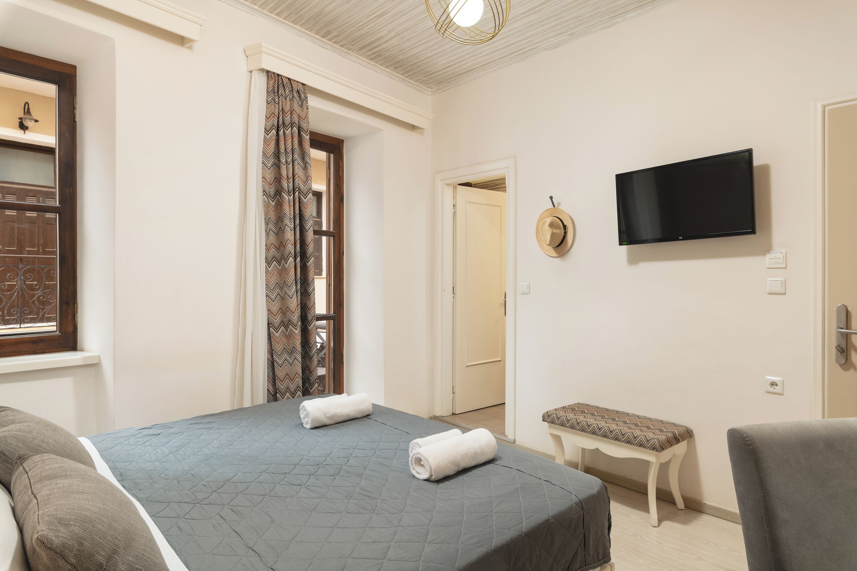 Een hotelkamer met een bed, een bankje, een televisie en een deur.