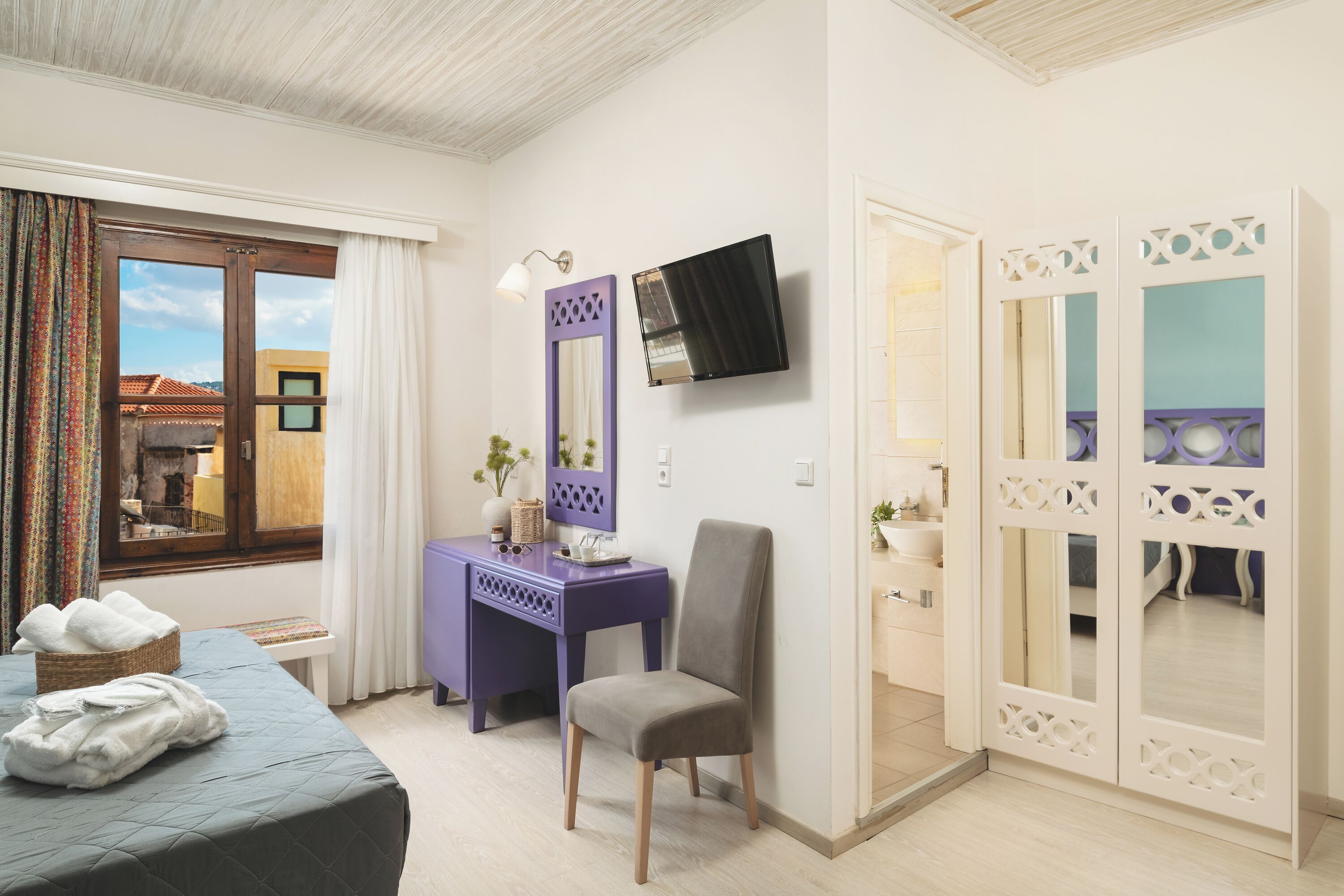 A hotel room with a bed, a desk, a chair, a TV, and a wardrobe.