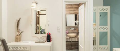 A bedroom with a bed, a desk with a chair, a mirror, and a bathroom visible through an open door.