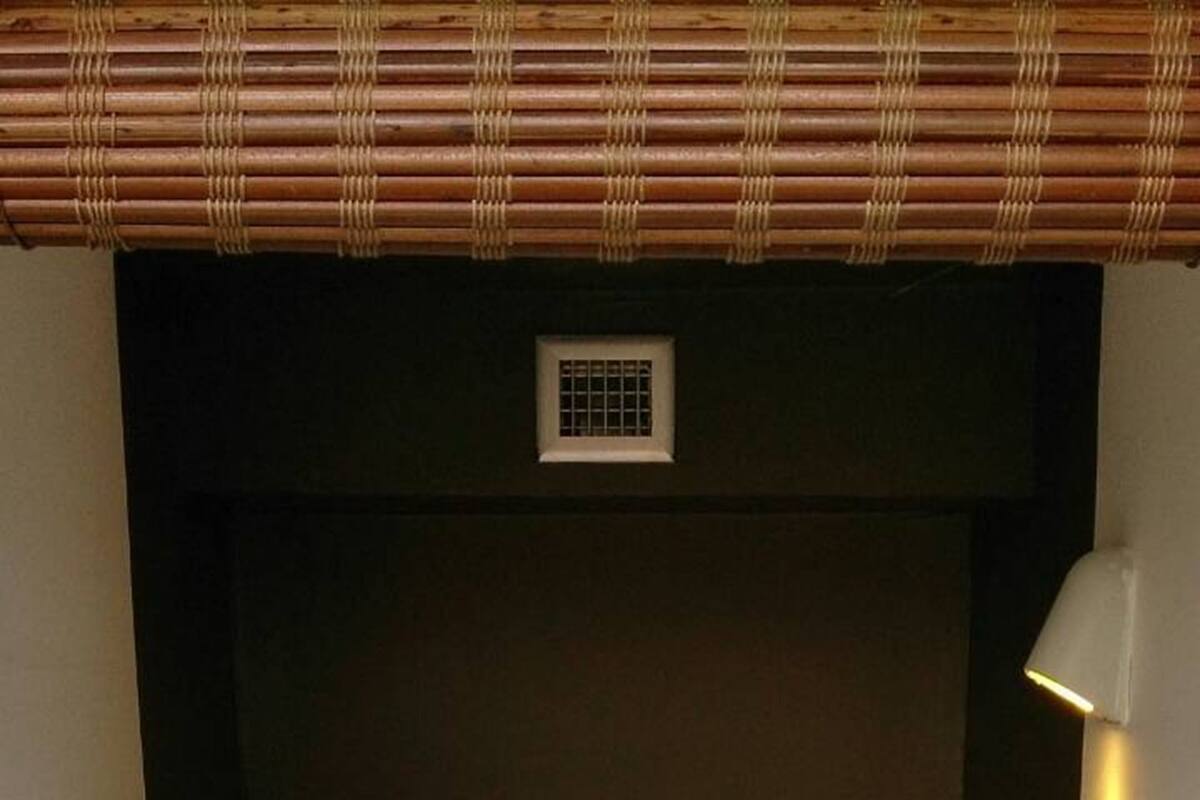 Una cama bien hecha con sábanas blancas y toallas enrolladas, un cabecero oscuro y una ventana pequeña con barrotes.