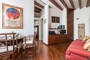 Una sala de estar con un sofá rojo, sillas de madera, una mesa de comedor y una cocina con mostrador y armarios de madera.