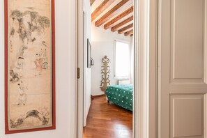 A room with a wooden floor, a bed with a green bedspread, a wall with a traditional painting, and a window with a white blind. - 7 Windows on Venice (Venice)