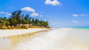 Een strand met helder turquoise water, wit zand en palmbomen.