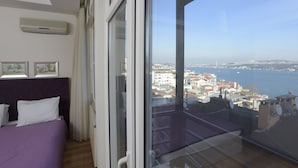 A balcony with a city view, a bed with a purple bedspread, and a ceiling fan. - Cheya Gumussuyu Residence (Istanbul)