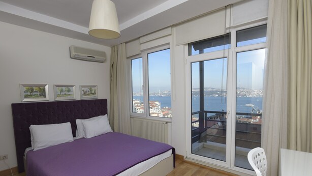 A bedroom with a large bed, a view of the city through a balcony, and a ceiling fan. - Cheya Gumussuyu Residence (Istanbul)