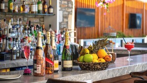 Een bar met verschillende drankflessen, een roze cocktail en een schaal fruit.