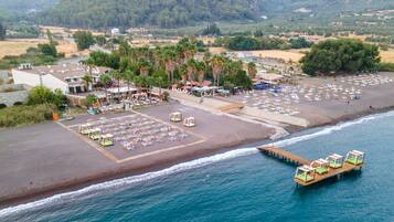 Vista aérea de un resort frente a la playa, con estacionamiento, sombrillas y un muelle de madera con sillas de descanso.
