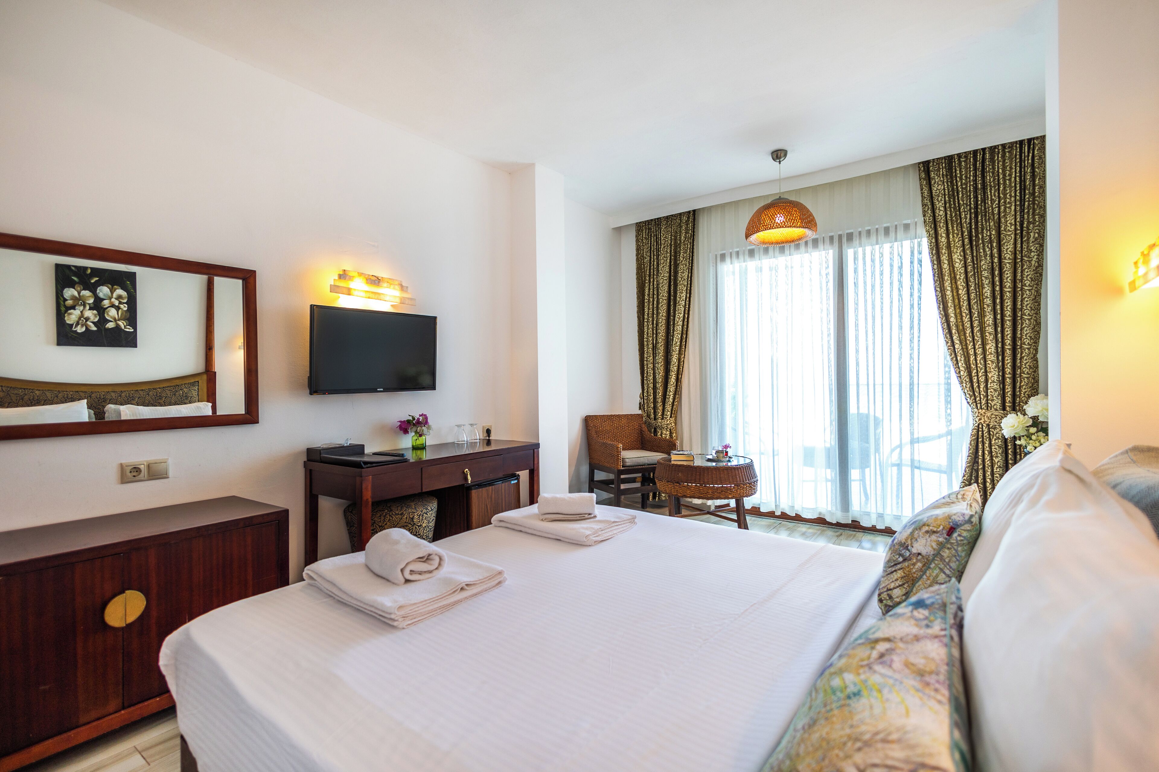 Una habitación de hotel con cama, escritorio, silla, televisor y ventana con cortinas.