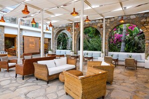 Un espace extérieur aménagé en terrasse, avec des meubles en osier, des murs en pierre et des guirlandes lumineuses.