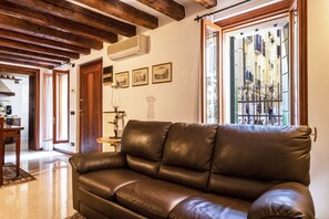 A living room with a brown leather sofa, wooden beams on the ceiling, and a view through a glass door to the outside. - Serenissima Authentic Venice (Venice)