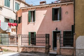 A pink building with green shutters, a metal gate, and a clothesline with red items. - Serenissima Authentic Venice (Venice)