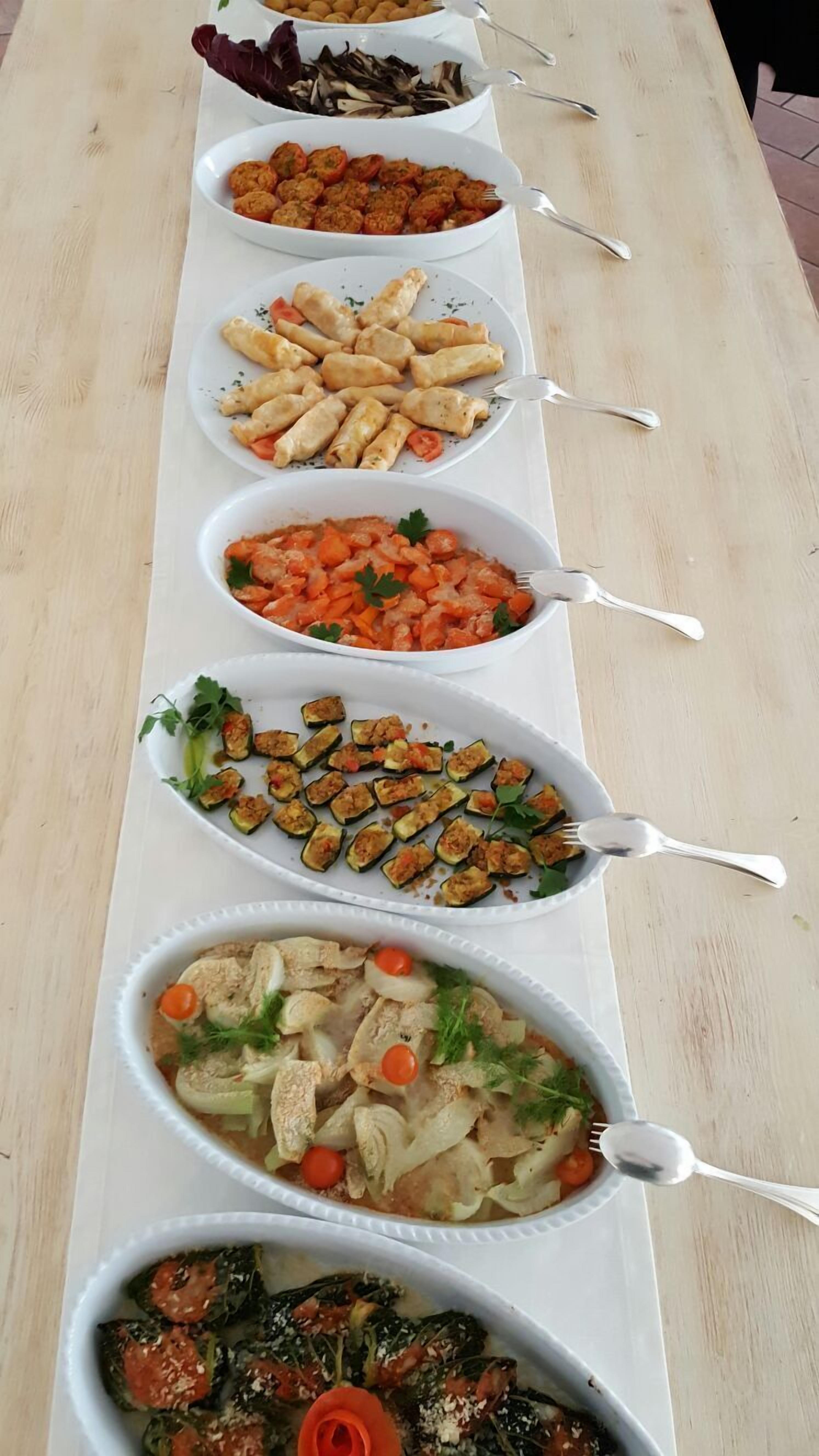 Une longue table est dressée avec de nombreux plats, comprenant des légumes et de la viande, présentés dans des bols blancs.
