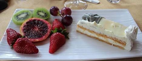 Un plato con postre, una porción de pastel de queso y diferentes frutas.
