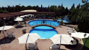 Un área de piscina con múltiples sillas de descanso y sombrillas, rodeada por un patio de ladrillo.