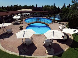 Un área de piscina con múltiples sillas de descanso y sombrillas, rodeada por un patio de ladrillo.