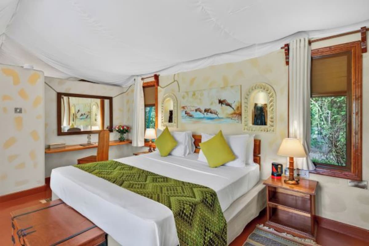 A hotel room with a large bed, a desk, a chair, a lamp, and a window with a view of trees.