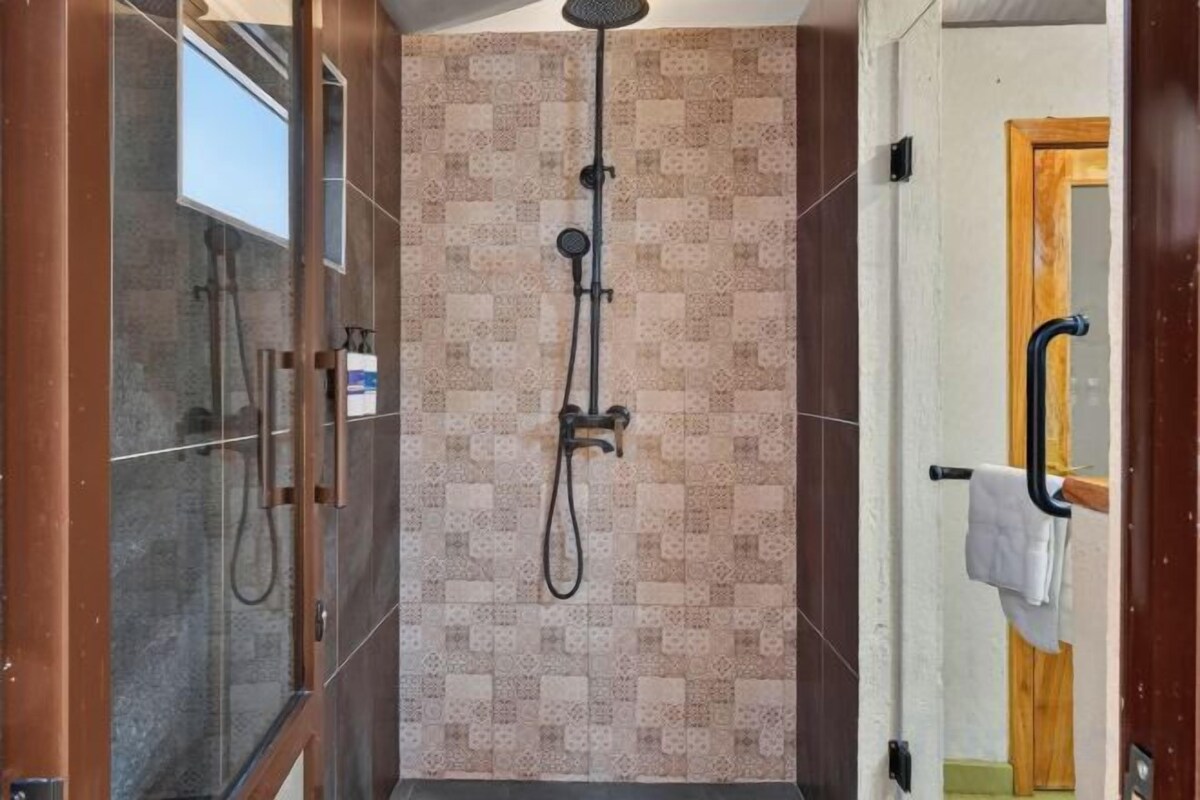 Zona de ducha con puerta de vidrio, cabezal de ducha y toallero.