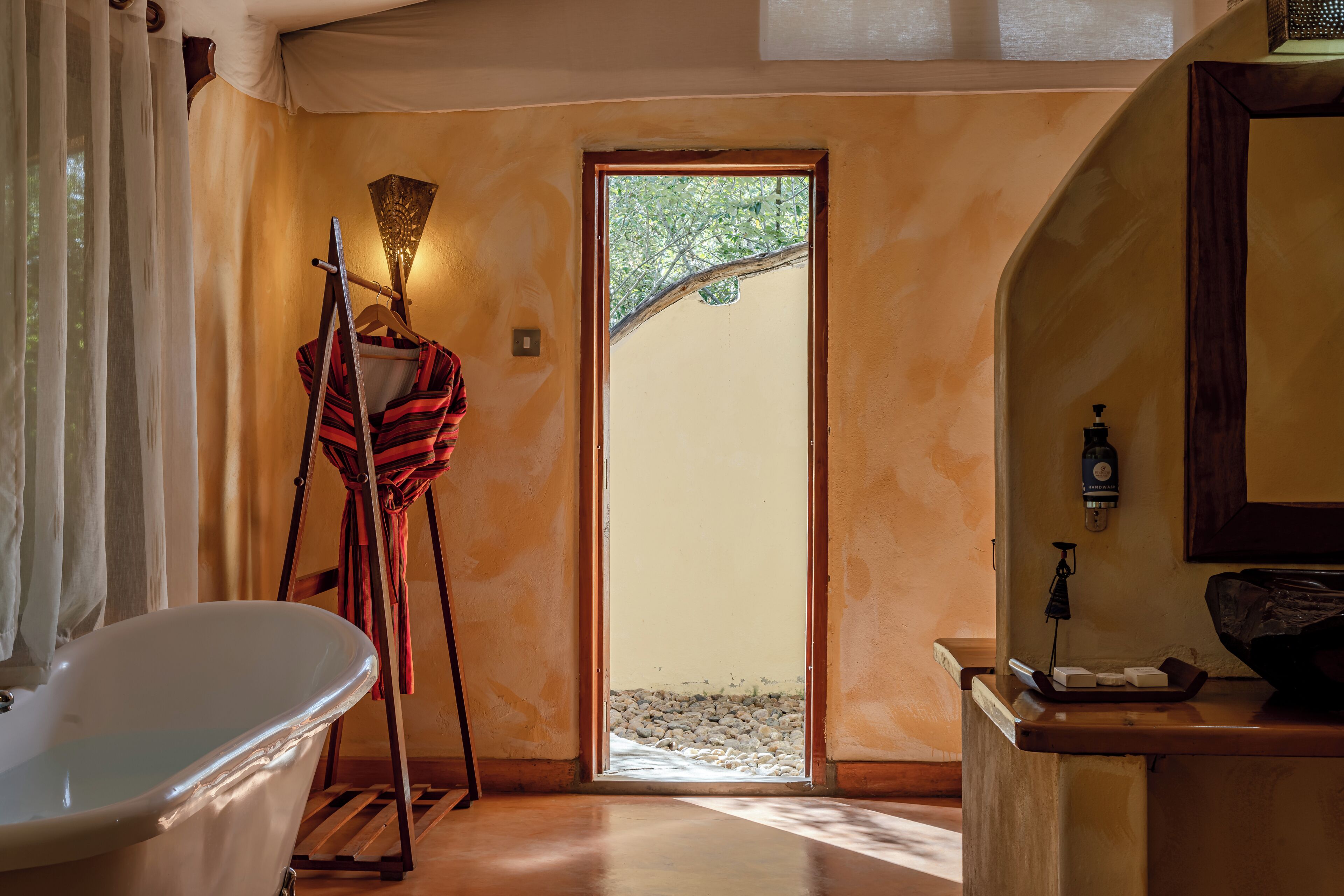Une salle de bain avec une baignoire sur pieds, un plancher en bois et une porte donnant sur un espace extérieur avec vue sur les arbres.