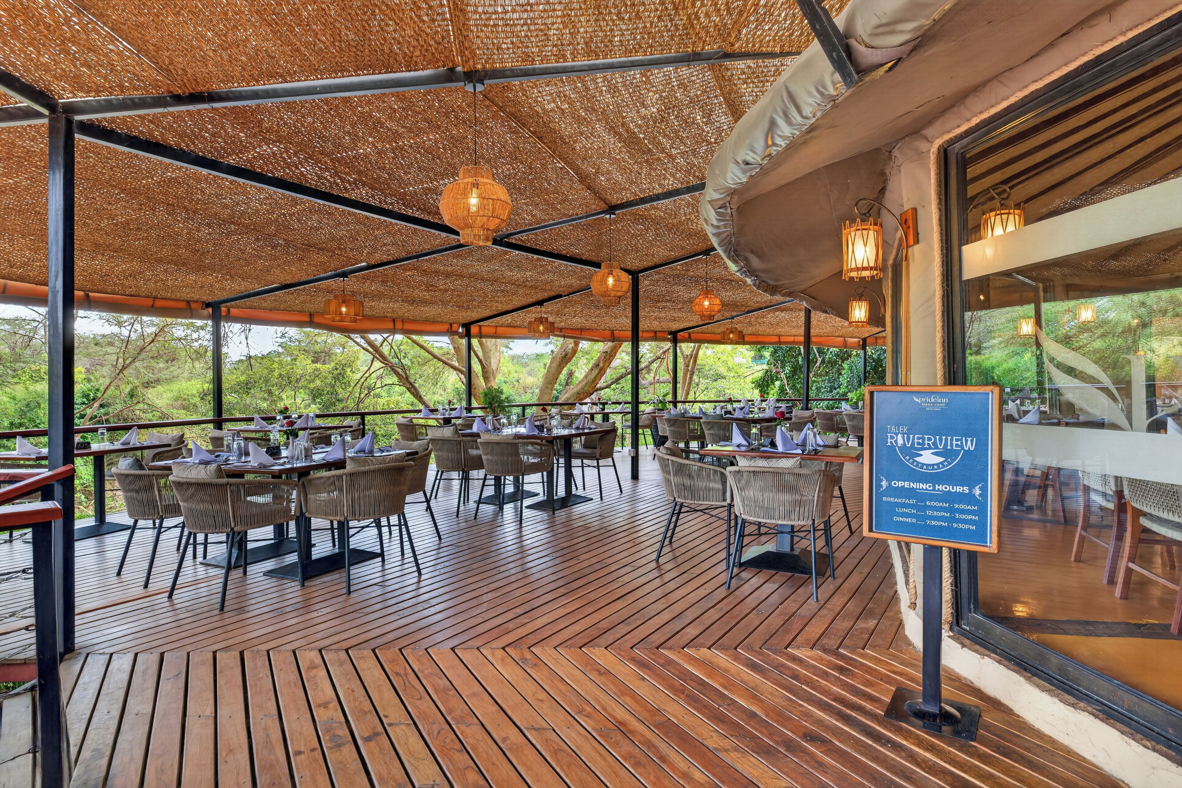 An outdoor dining area with tables and chairs, a thatched roof, and hanging lights.