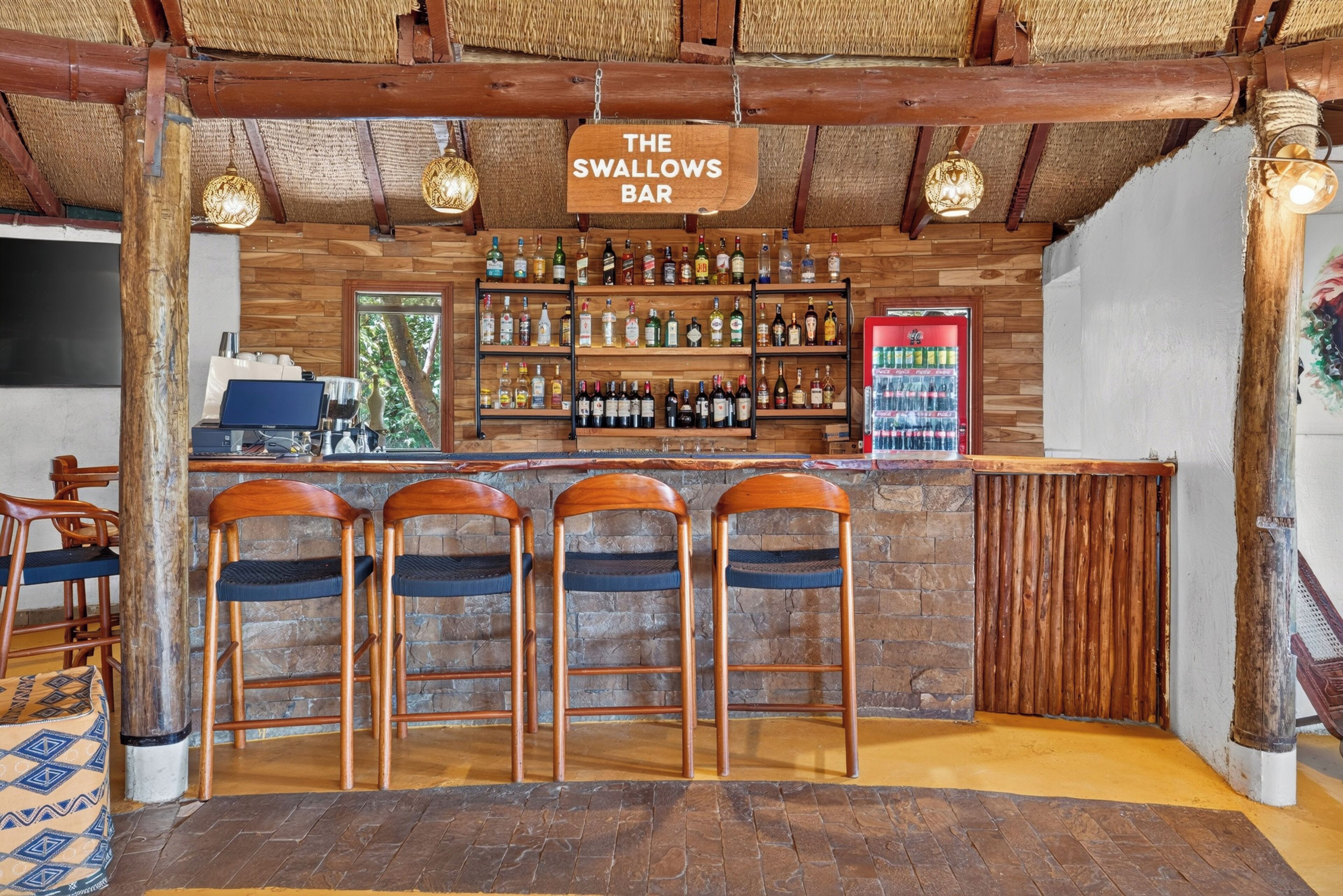 Zona de bar con taburetes de madera, barra y estanterías llenas de botellas.
