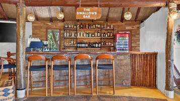 Zona de bar con taburetes de madera, barra y estanterías llenas de botellas.