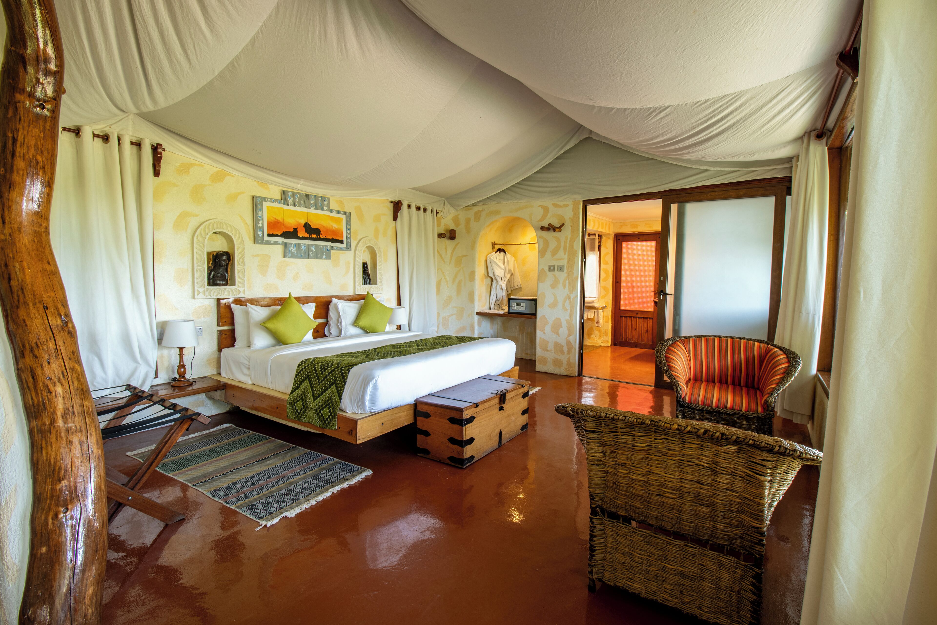 A spacious bedroom with a large bed, a sitting area with a wicker chair, and a view of the bathroom.