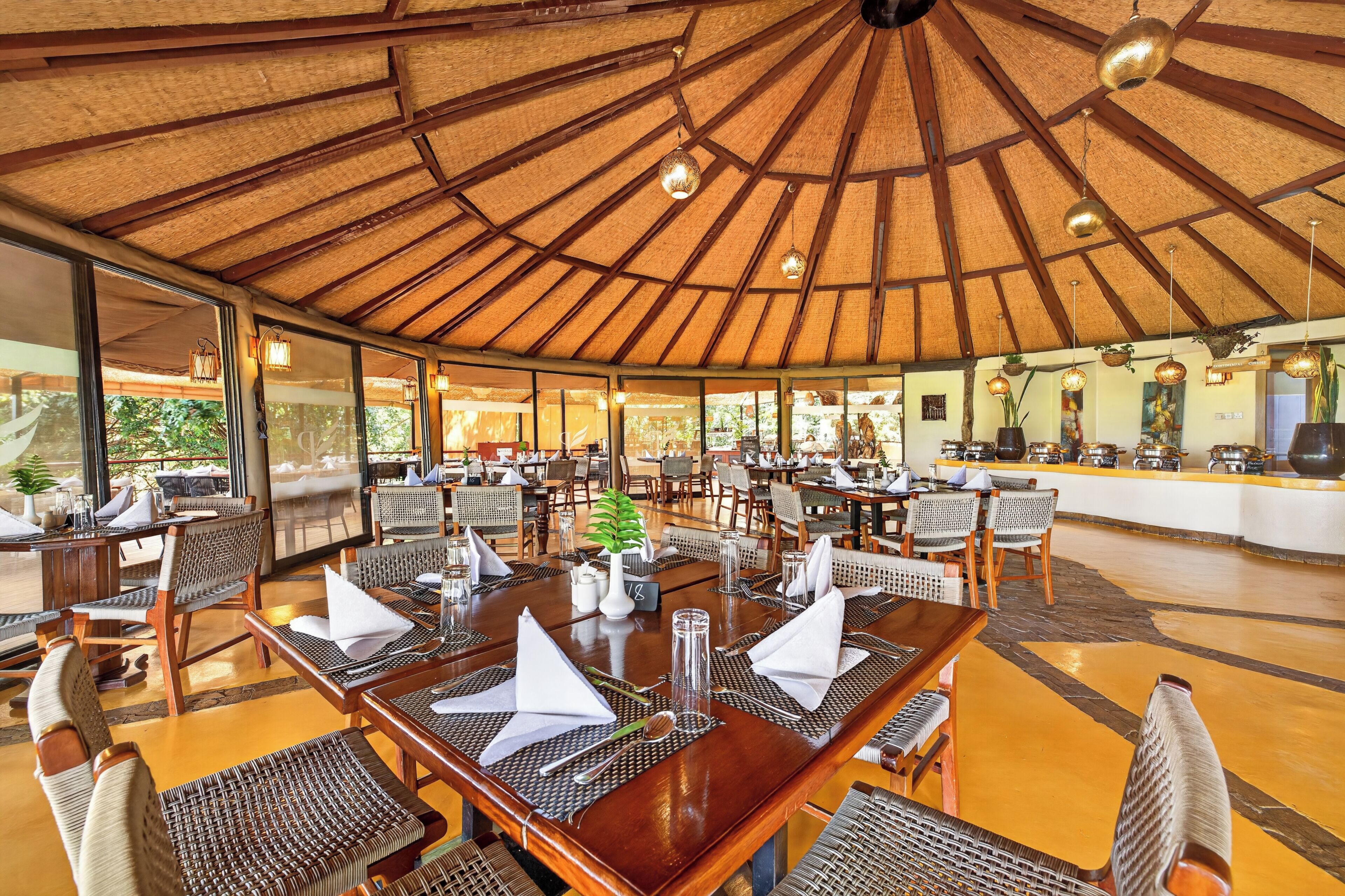 A restaurant with a thatched roof, wooden tables, and wicker chairs.