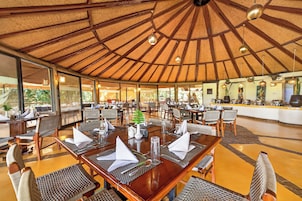 Un restaurante con techo de paja, mesas de madera y sillas de mimbre.