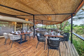 An outdoor dining area with wooden flooring and wicker furniture, covered by a woven canopy. - PrideInn Mara Camp & Cottages (Maasai Mara)