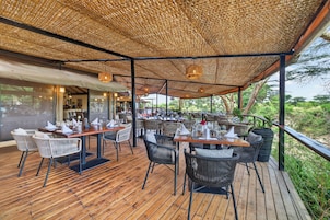 Un área de comedor al aire libre con piso de madera y mobiliario de mimbre, cubierta por un dosel tejido.