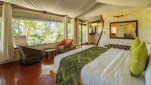 Une chambre spacieuse avec un grand lit, un coin salon avec un fauteuil et une vue sur l’extérieur.