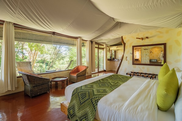 A spacious bedroom with a large bed, a sitting area with a chair, and a view of the outdoors. - PrideInn Mara Camp & Cottages (Maasai Mara)