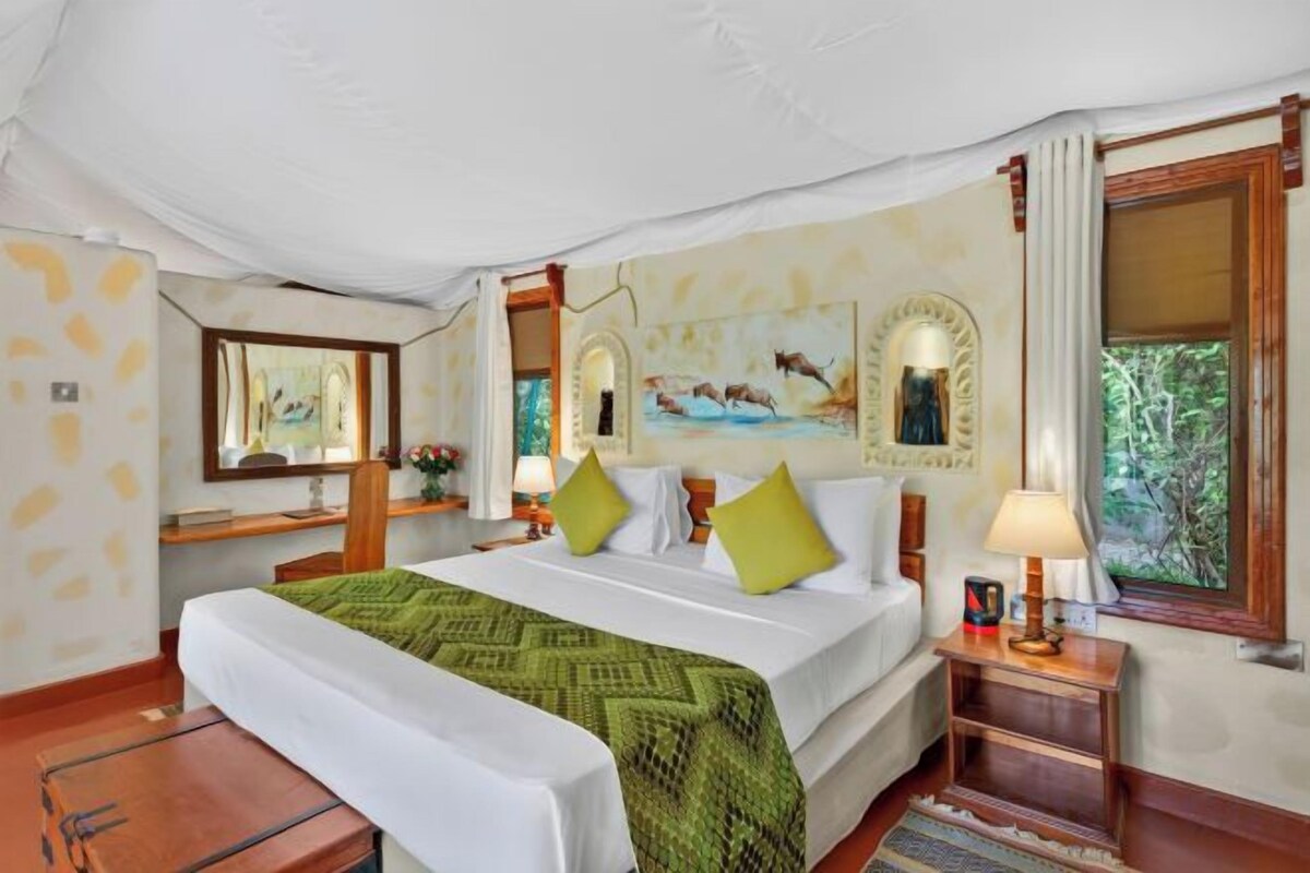 Una habitación de hotel con una cama grande, un escritorio con silla, un espejo y una ventana con cortinas.