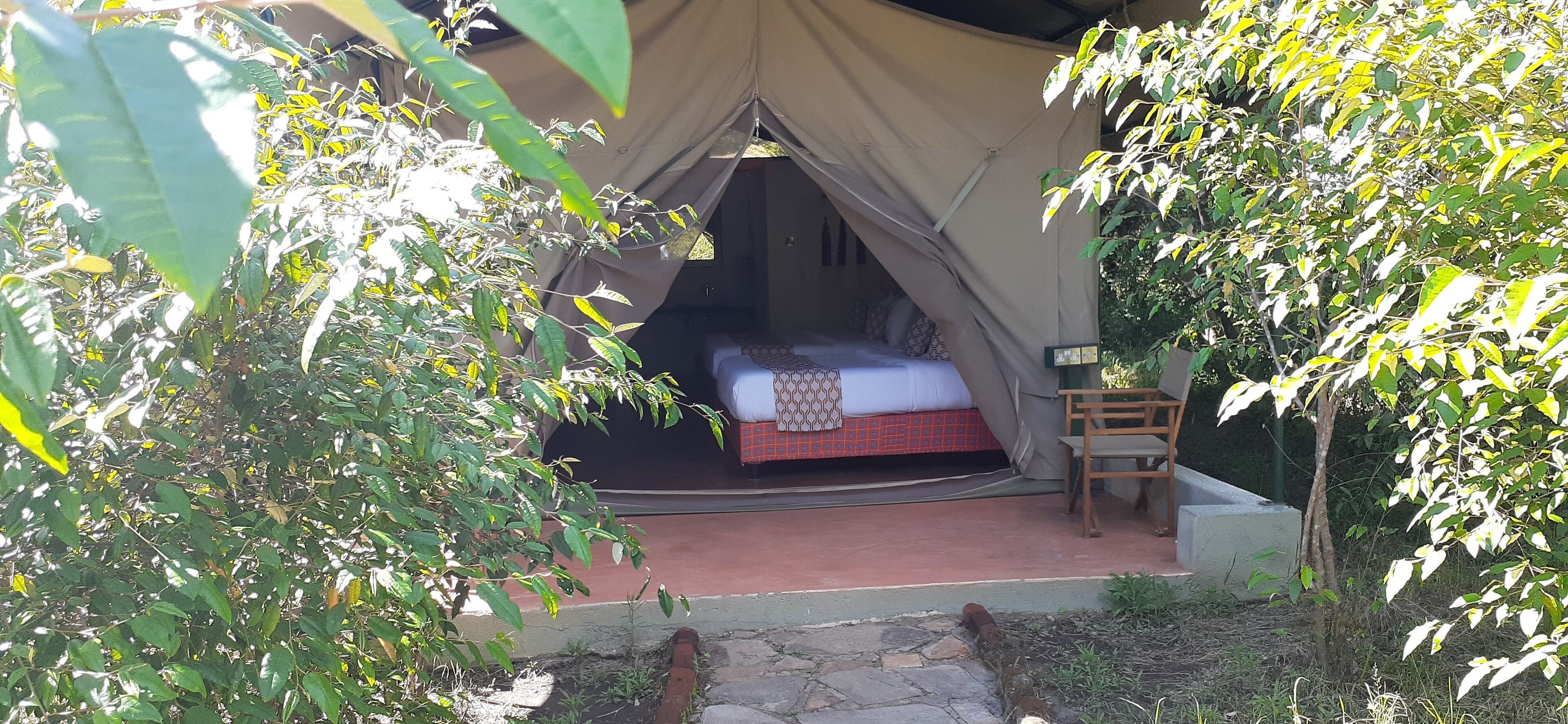 A tented accommodation with a bed, a chair, and a small table.