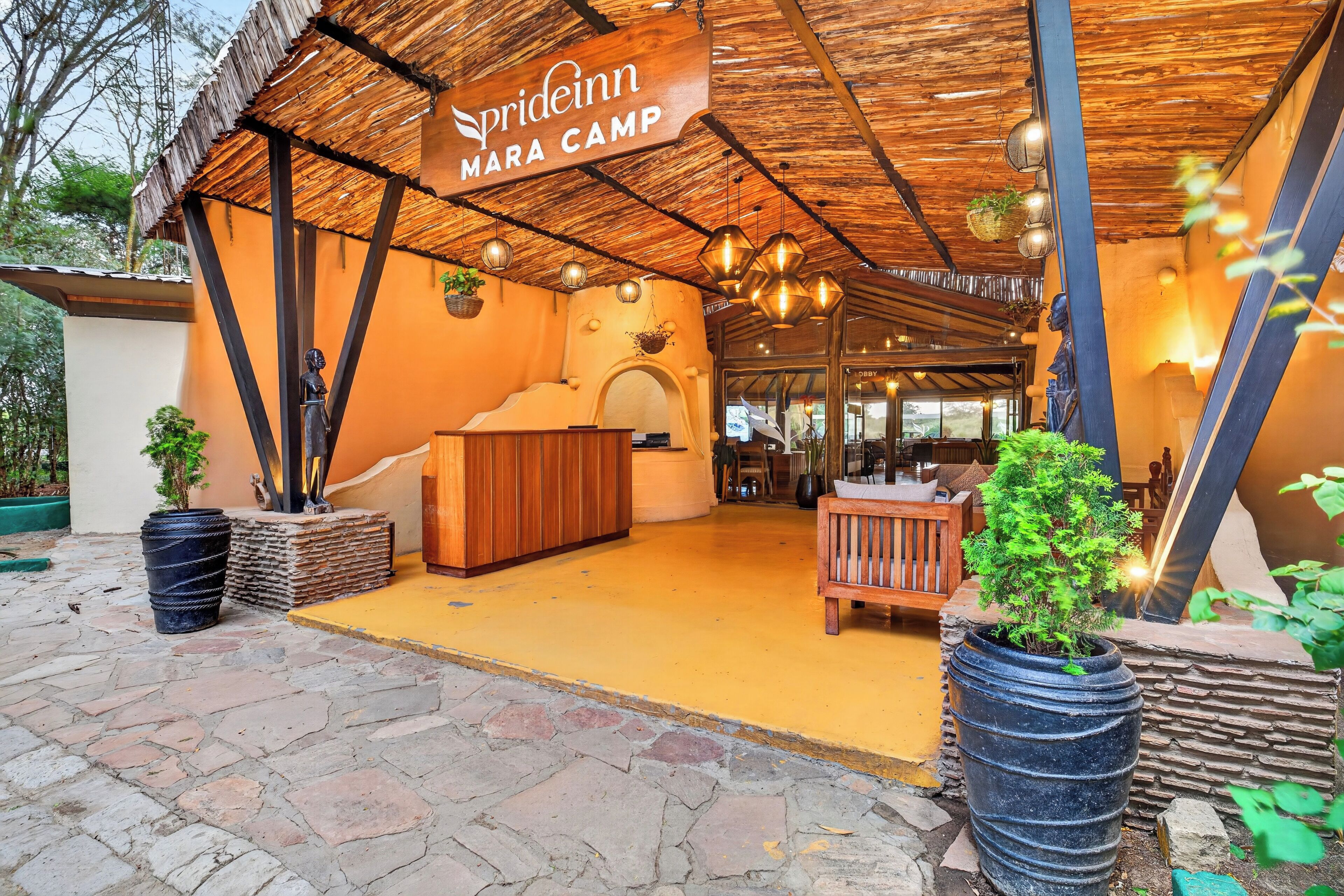 A camp with a thatched roof, wooden furniture, and potted plants.