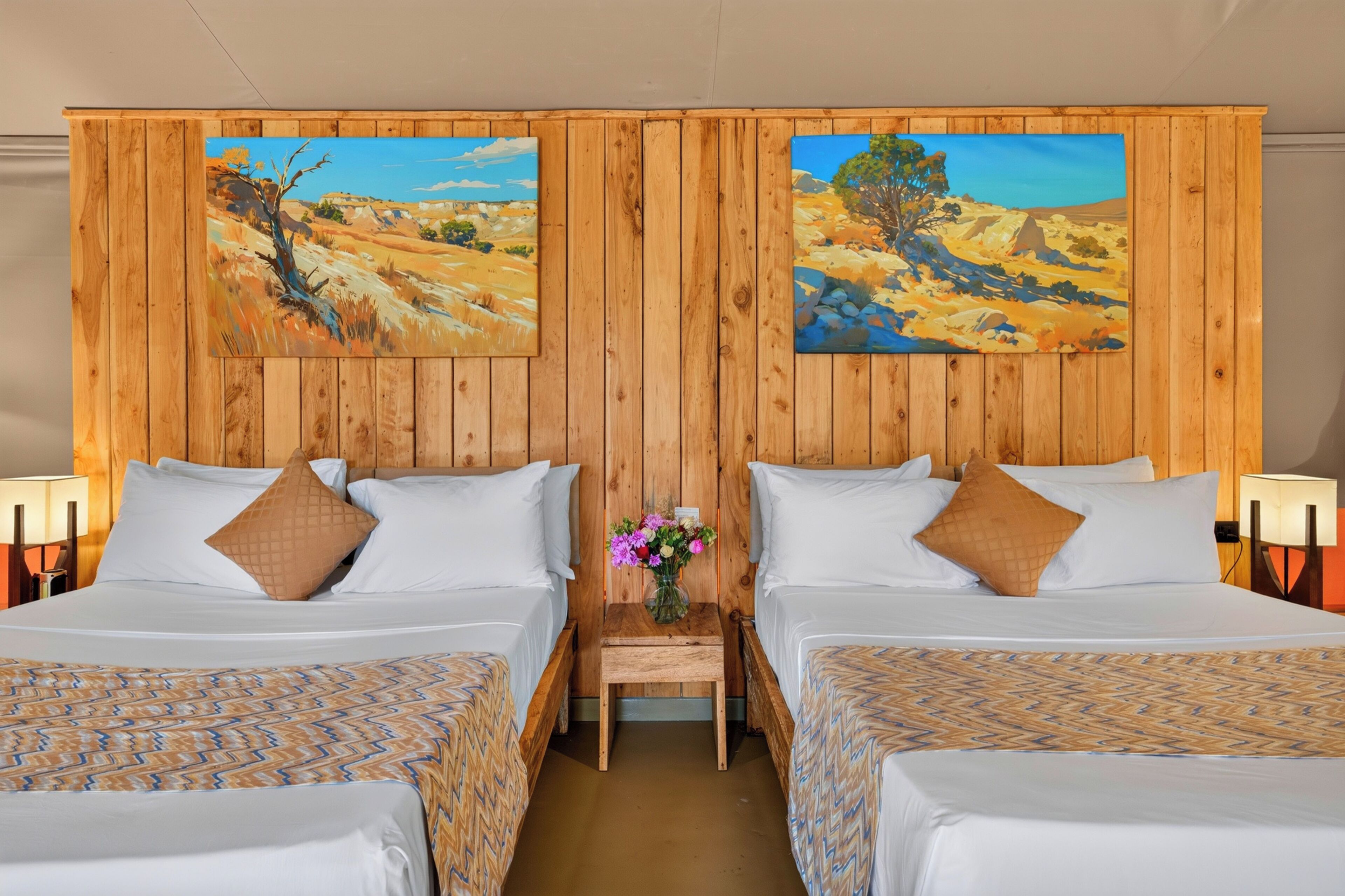 A hotel room with two beds, wooden headboard, and two paintings.