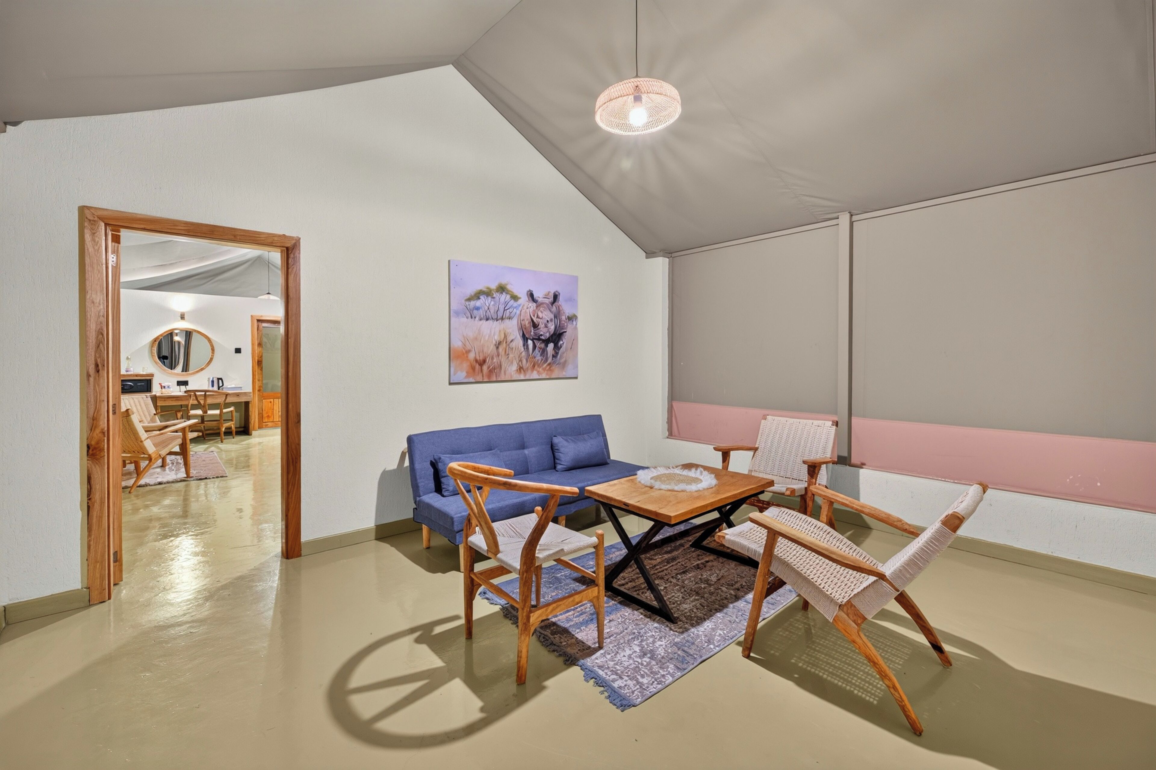 Una habitación con un sofá azul, sillas de madera, una mesa, un cuadro y una lámpara en el techo.