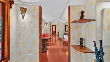 A corridor with a patterned wall, a red chair, a wooden shelf with an umbrella, and a small statue.