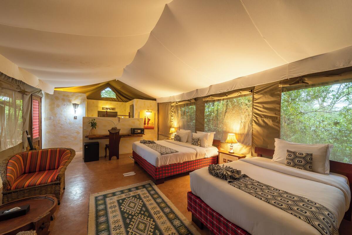 A tented room with two beds, a sofa, a desk, and a chair.