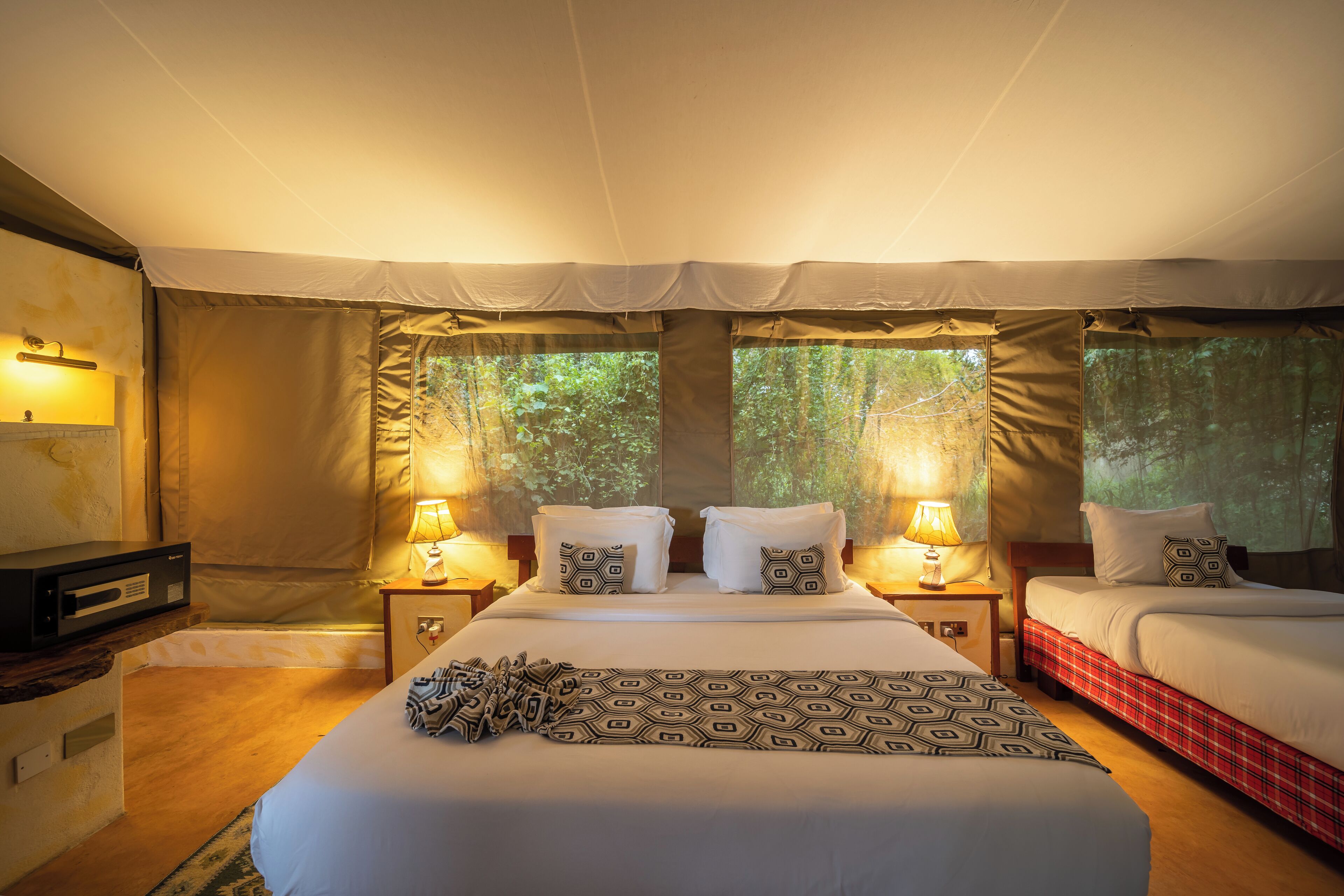 A tented room with two beds, each with a pillow and a lamp.