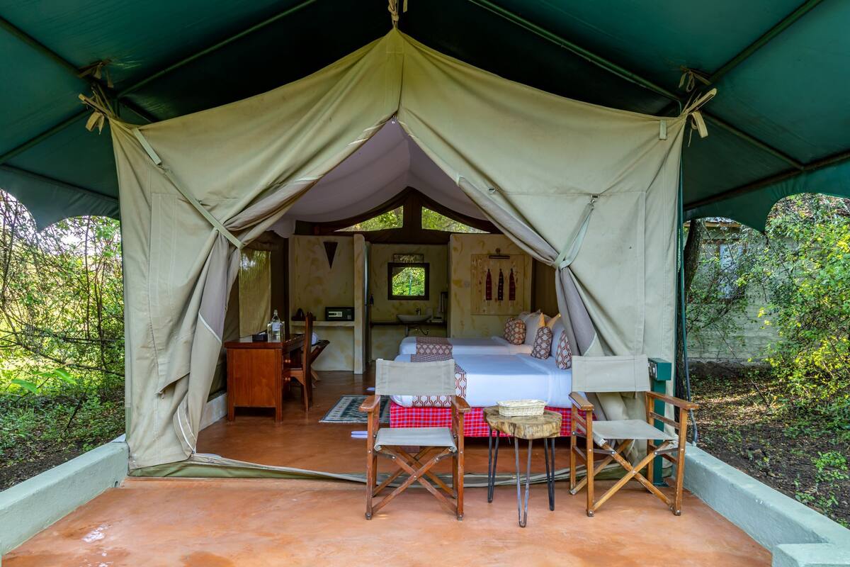 A tented accommodation with a bed, a table, and chairs.