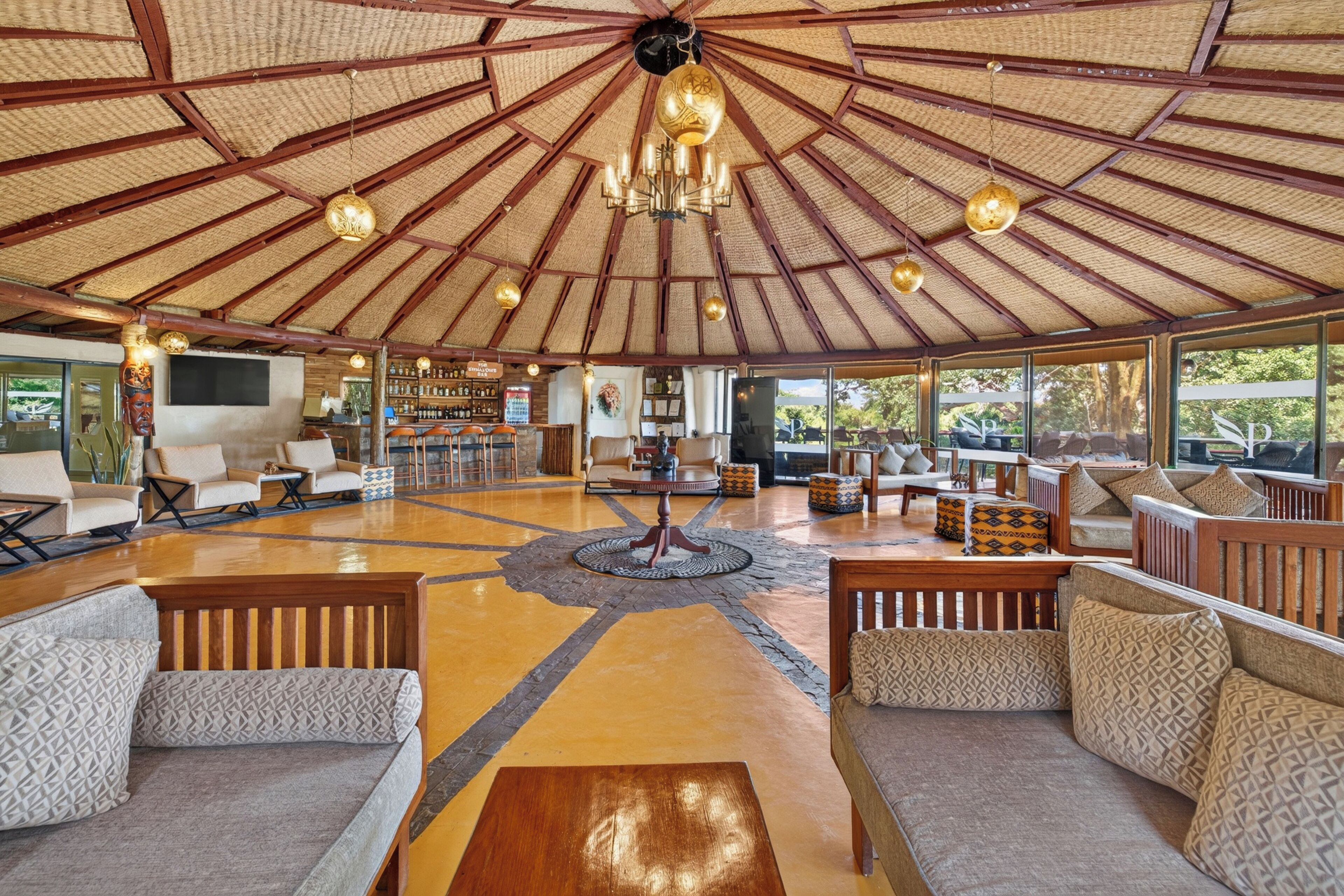 A spacious lounge area with a high ceiling and a central chandelier, surrounded by comfortable seating and a bar area.
