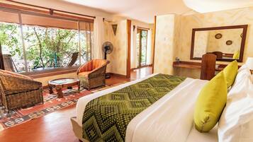 A room with a bed, a chair, a fan, and a window with a view of trees.