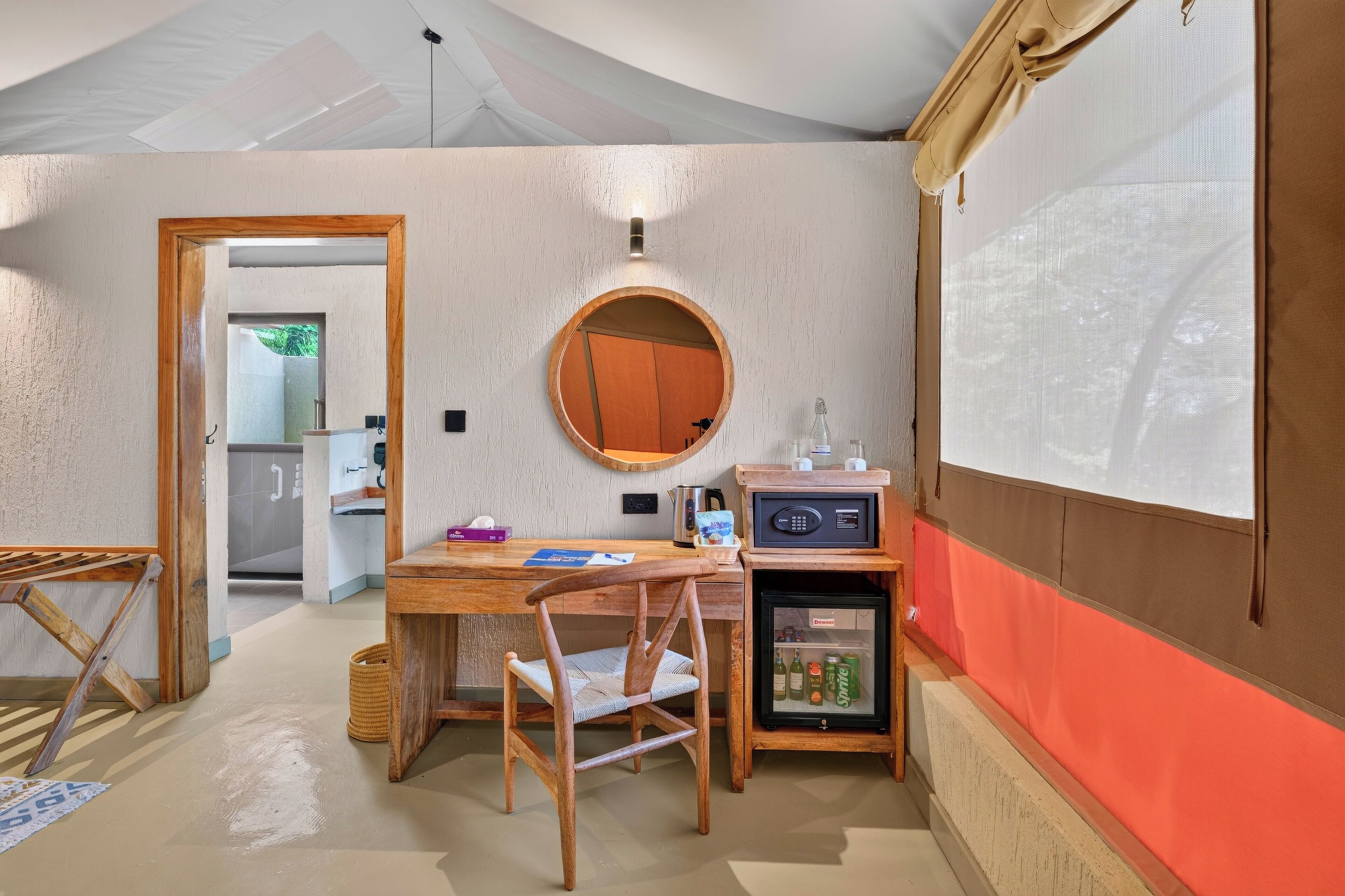 Ein kleines Zimmer mit einem Holztisch, einem runden Spiegel, einem kleinen Kühlschrank und einem an der Wand montierten Fernseher.
