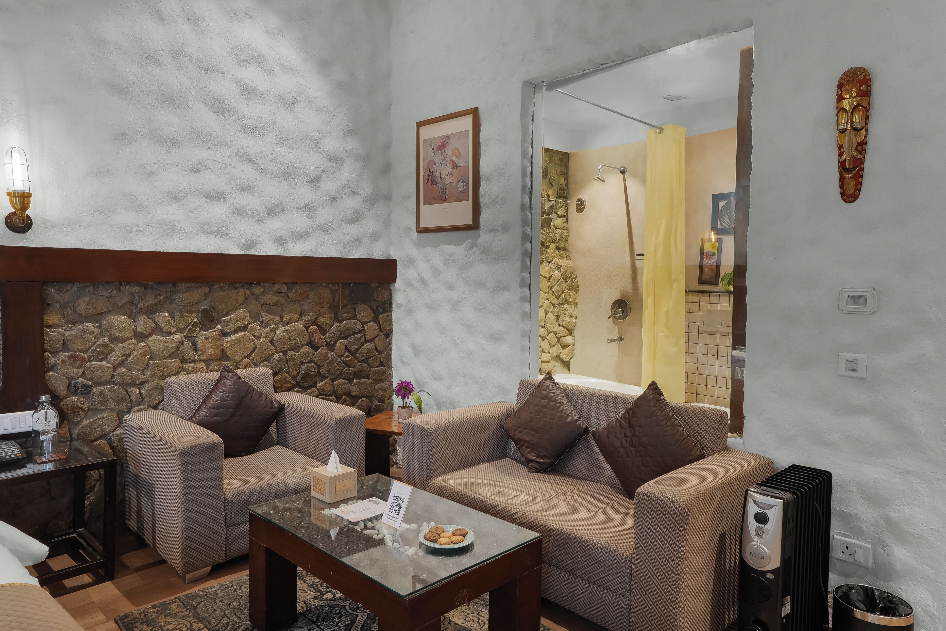 A living room with a stone fireplace, two sofas, a coffee table, and a small table with a bottle and tissues.