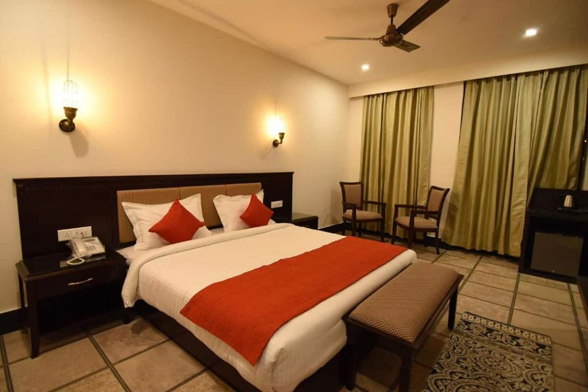 Quarto de hotel com cama, mesas de cabeceira, escrivaninha, cadeira, ventoinha no teto e cortinas.